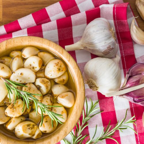 Aged garlic on a bowl with oil and raw garlic on the wooden table with striped table cloth