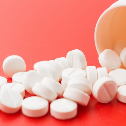 Tablets of aspirin in white with white bottle in red background